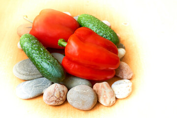 Two red sweet peppers, two green cucumbers on stones