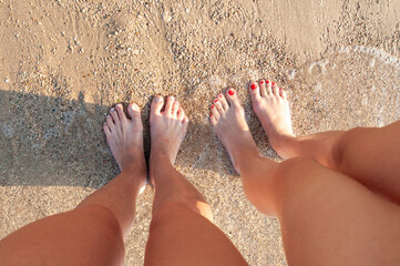 Women's legs standing on the beach.