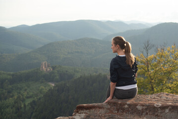 Naklejka premium Travel. A girl sits on the edge of a cliff, admiring the view of the mountains. A journey, a walk in nature.