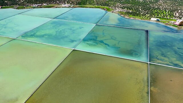 Aerial footage of surface of salterns evaporation ponds or saltworks evaporation fields under sun
