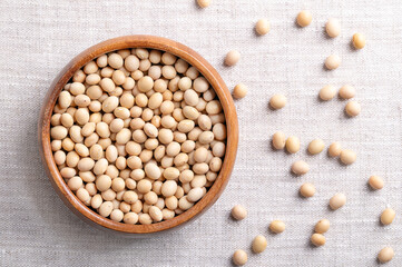 Dried soybeans, also soy beans or soya beans in a wooden bowl on linen fabric. Whole and raw seeds of the legume and oilseed Glycine max, with a very high protein and oil content. Close-up from above.