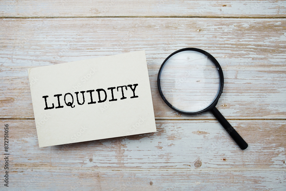 Poster liquidity text message and magnifying glass with space copy on wooden background