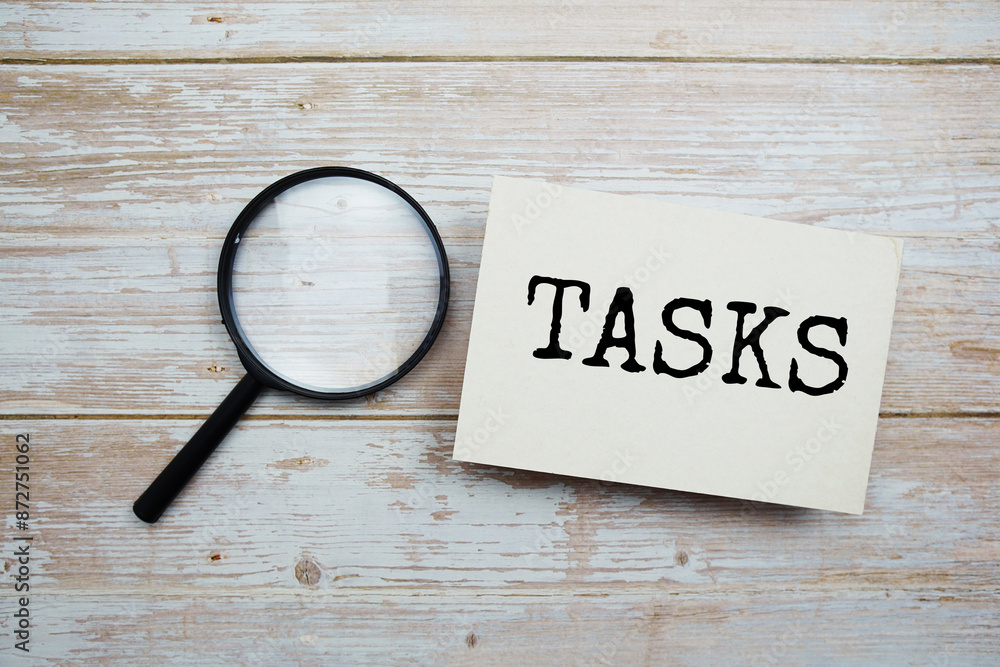 Poster tasks text message and magnifying glass with space copy on wooden background