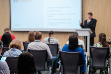 Audience attentively listening to a speaker presenting at a tech conference. Presenter in the background, highlighting modern business and technology topics.