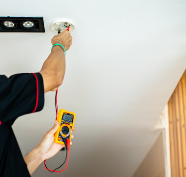 Close-up of technicians using a digital multimeter to test voltage on a fire alarm system installation.