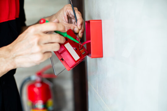 Close-up of technician hands installing and wiring a red fire alarm manual call point box on a wall.