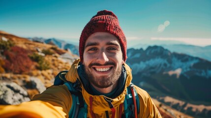 Naklejka premium A cheerful young hiker smiles for the camera as he takes a selfie on a mountaintop surrounded by beautiful scenery.