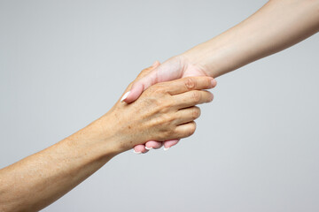 The hand of a young girl holds the hand of an elderly woman, isolated on a light gray background. The concept of caring for retired parents. Helping hand. Support for people with aging diseases
