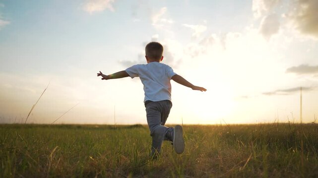Happy child playing outside. Boy imagines being airplane on meadow. Carefree childhood child running freely. Scenic sunset joyful play concept. Happy Child enjoys nature playing airplane in meadow.
