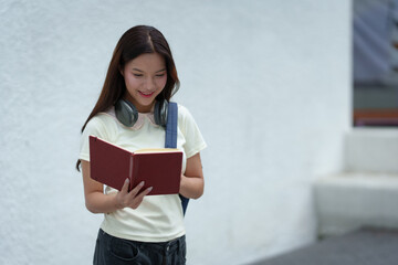 Attractive Asian female student standing holding a backpack and textbooks Smiling and looking at the camera while leaning against the background. learning concept new study online teenagers.