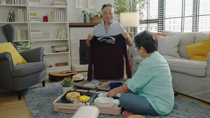 Asian romantic retired couple packing clothes travel bag suitcase together on floor in living room at home.senior Asian couple travel weekend,after retirement,happy insurance,good healthcare concept. - Powered by Adobe