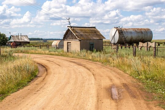 Rural scene with a dirt road that leads to a small, abandoned-looking house