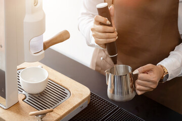 Female barista in apron using blender to froth milk Making coffee for customers in a coffee shop ,small business idea