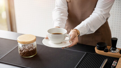 Female barista holding a coffee cup on the counter working in a coffee shop. Service, small business.