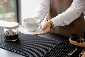 Female barista holding a coffee cup on the counter working in a coffee shop. Service, small business.