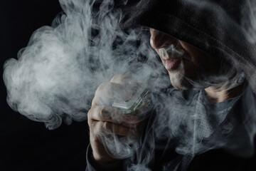 a man smokes a vape electronic cigarette in black clothes on a dark background, close-up