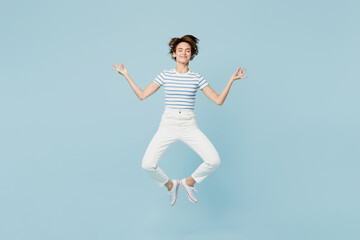 Obraz premium Full body young woman wears striped t-shirt casual clothes jump high hold spreading hands in yoga om aum gesture relax meditate try to calm down isolated on plain blue background. Lifestyle concept.