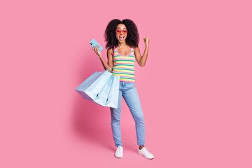 Full size photo of excited woman dressed knit tank in glasses hold shopping bags smartphone win betting isolated on pink color background