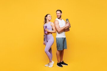Fototapeta na wymiar Full body side view young strong fitness trainer sporty two man woman wearing blue clothes spend time in home gym hold bottle drink water isolated on plain yellow background Workout sport fit concept