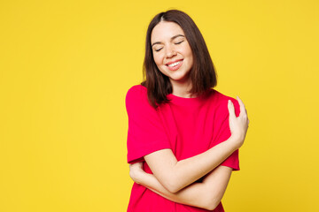 Obraz premium Young smiling happy cheerful fun cool woman she wearing pink t-shirt casual clothes hold hug embrace herself, close eyes isolated on plain yellow orange background studio portrait. Lifestyle concept.