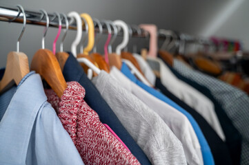 Clothes hanging in closet, several pieces on each hanger. Inconvenient way of storing clothing, challenge of organizing and accessing garments efficiently