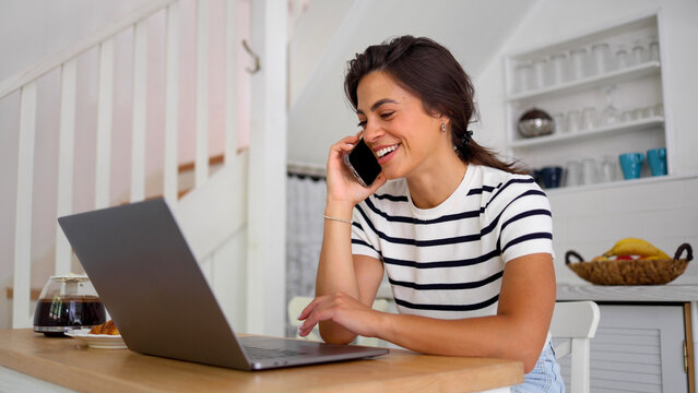 Young woman working online at her home office and talking on mobile phone