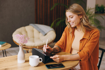 Young IT woman wear shirt hold use digital tablet pc computer use write draw stylus pc pen sitting...