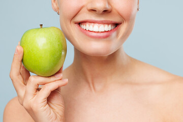 Close up cropped happy half naked topless young woman 20s with nude make up hold in hand green apple isolated on plain pastel blue color background. Skin care healthcare cosmetic procedures concept.