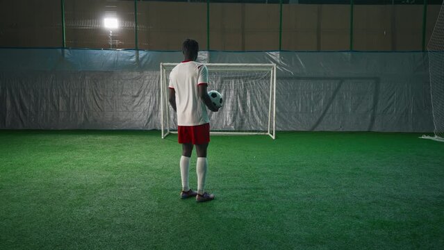 Black soccer player exercising penalty in training hall, scoring goal, back view