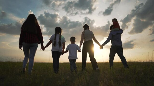 Happy group people walking outdoors at sunset. Family unity friendship in nature. Silhouette happy group enjoying scenic walk. People bonding and holding hands. Togetherness and joy in group setting.