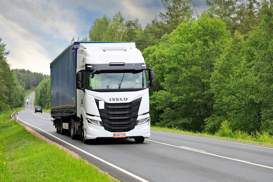 White Iveco S-Way truck pulls curtainside semi trailer uphill along highway on a day of summer. 
