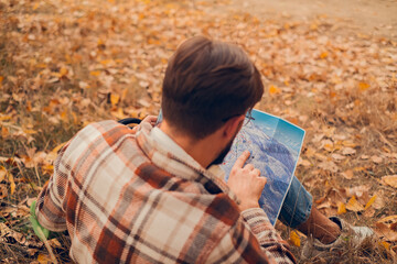 Fototapeta premium Back view of a man in a plaid shirt holding a map of wooded terrain, engaged in sports activities like orienteering and trail running, emphasizing navigation and route planning.