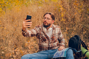Young male blogger relaxing in nature away from the city, creating vlogs about hiking using his smartphone.