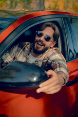 A bearded man in glasses peers out the front window of a car, adjusting the rearview mirror, emphasizing the importance of road safety