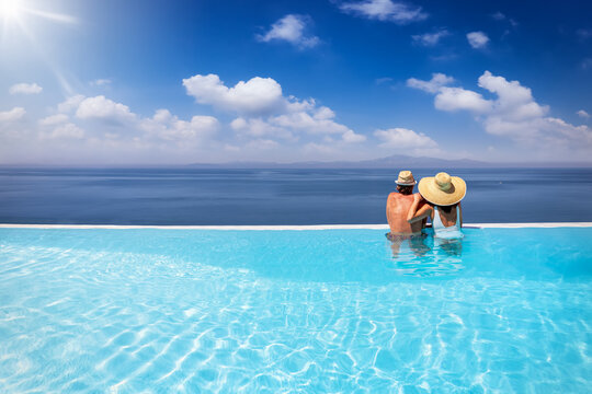 A holiday couple in a big infinity pool enjoys the panoramic view to the blue sea during summer vacation time