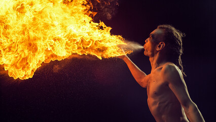 Male Fire Performer With Dreadlocks Skillfully Exhales Massive Fireball, Creating Spectacular...