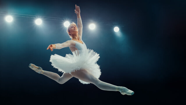Elegant Ballet Dancing Ballerina White in Tutu Executes Flawless Grand Jet&eacute; Under Bright Stage Lights, Capturing the Grace and Precision of Classical Ballet in Stunning Performance.