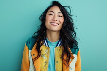 Portrait of a happy asian woman in her 40s sporting a stylish varsity jacket isolated on soft teal background