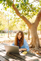 Young woman sits in park with laptop. Remote work or education.  Freelance, online course.