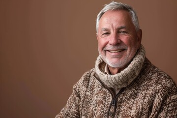 Fototapeta premium Portrait of a happy man in his 60s dressed in a warm wool sweater in soft brown background
