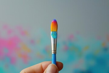 A hand holding a small paintbrush with colorful bristles, set against a high-key, minimalistic background, creating a striking visual contrast.