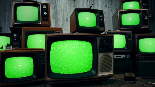 Multiple retro televisions with green screens in dark room