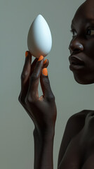 Portrait of a black beauty model balancing an egg shaped object on her fingertips, orange nail polish