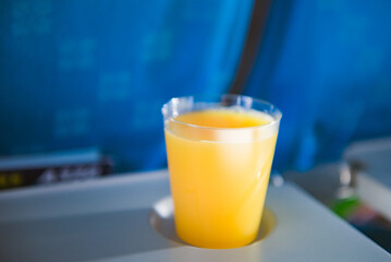 A cup of orange juice on tray at cabin seat of an aircraft.	