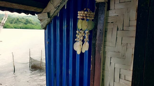 Close up to a wind chime made from capiz swaying wildly in the breeze and hanged on a native hut overlooking the sea, candid island living moment