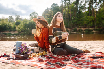 Fall picnic on the beach. Stylish women enjoying autumn weather on coastline. People, lifestyle, relaxation and vacations concept.