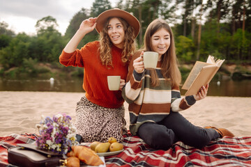 Fall picnic on the beach. Stylish women enjoying autumn weather on coastline. People, lifestyle, relaxation and vacations concept.