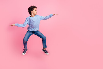 Full length photo of attractive funny grandson wear blue pullover jumping high showing arm emtpy space isolated pink color background