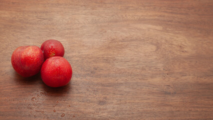 Three pieces of fresh Cherry Plum (Prunus cerasifera) fruits are arranged on a wooden background.