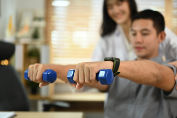 Athlete male patient lifting weights dumbbell under physiotherapist guidance. Rehabilitation and health care concept